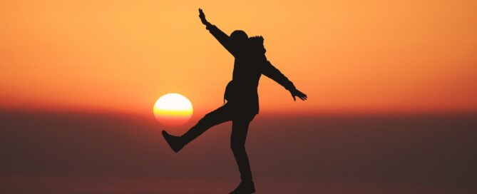 A person standing on a rock in front of a sunset